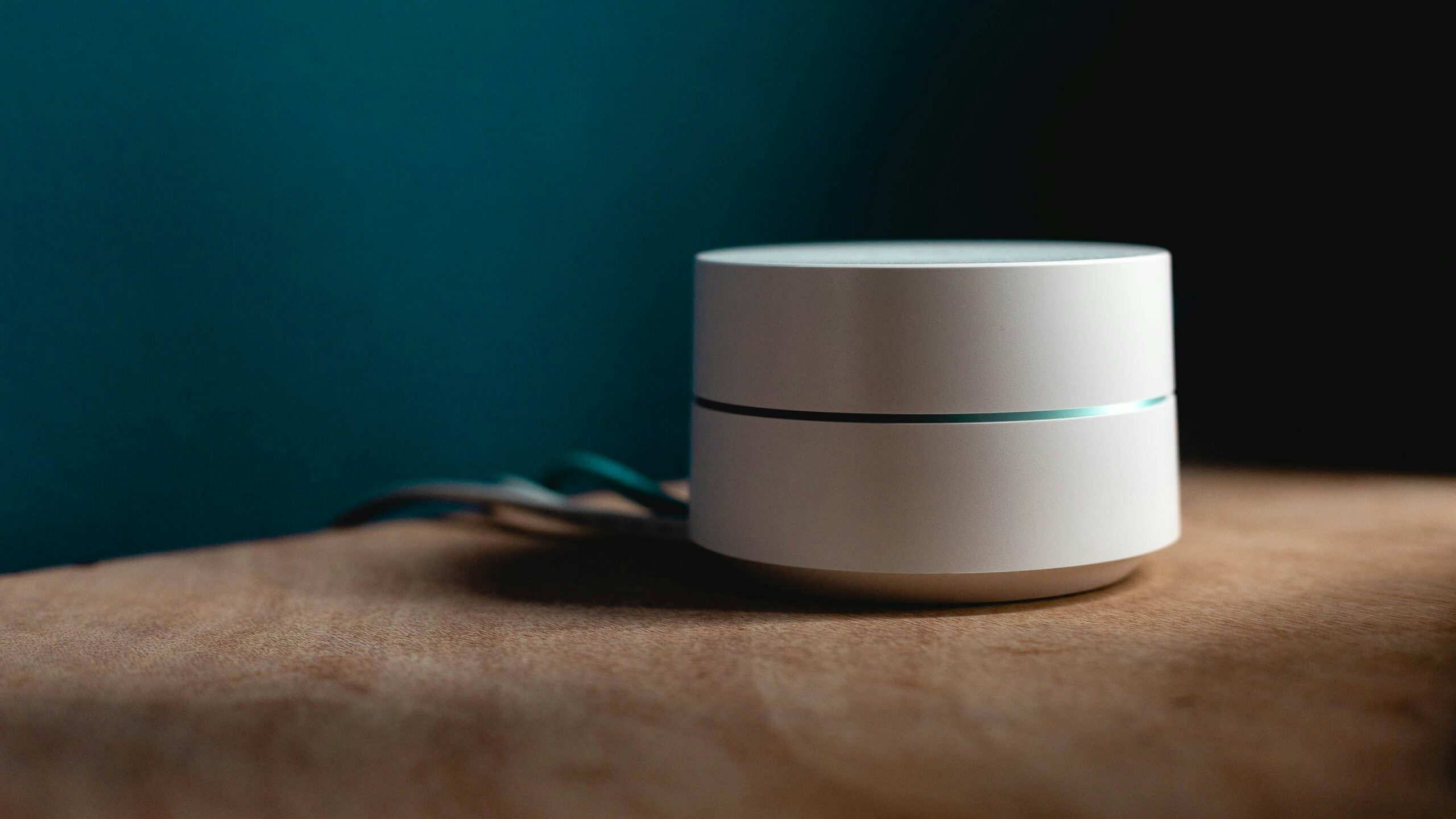 Smart speaker on a wooden table against a dark teal background.