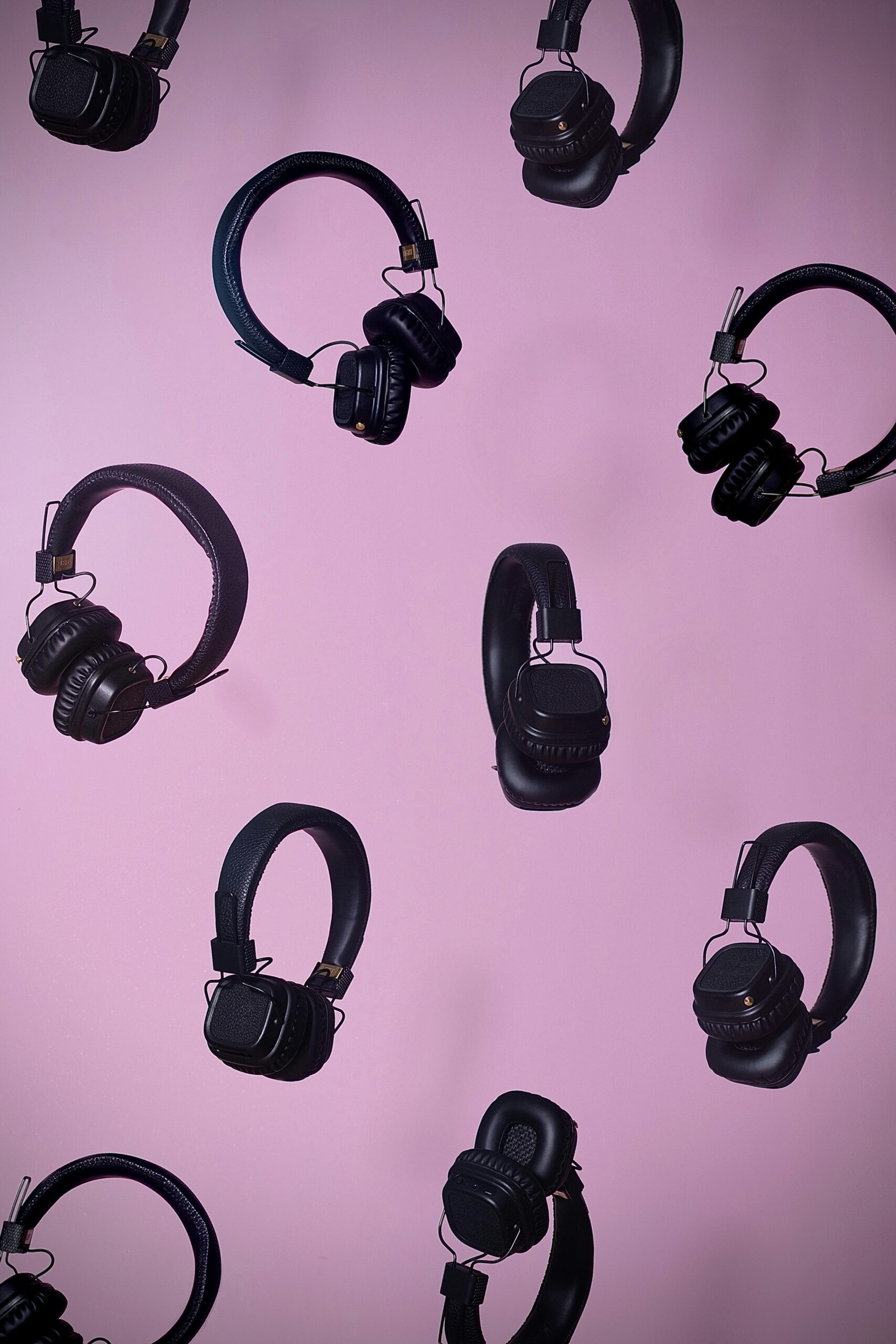 A group of black headphones on a pink background.