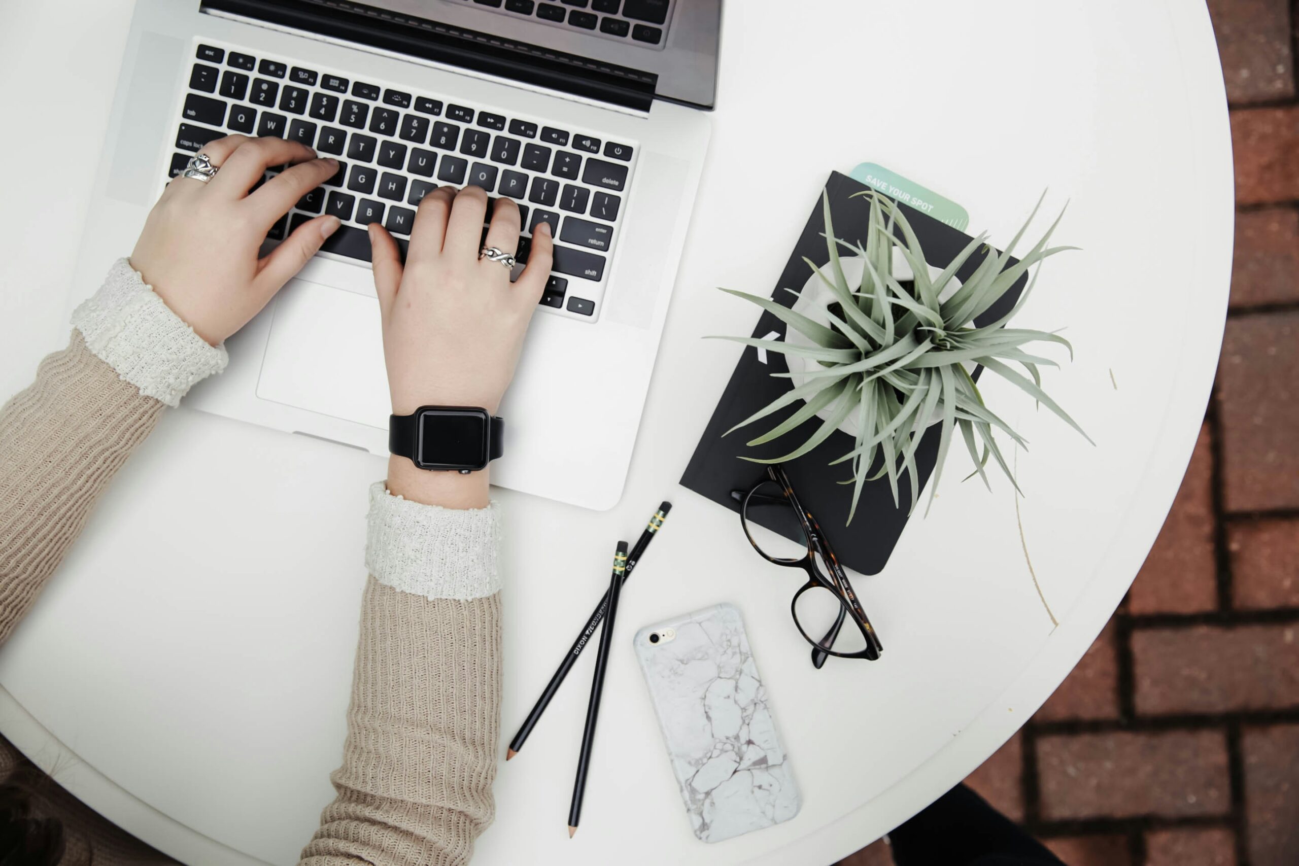 A woman typing on a laptop with a plant in the background.