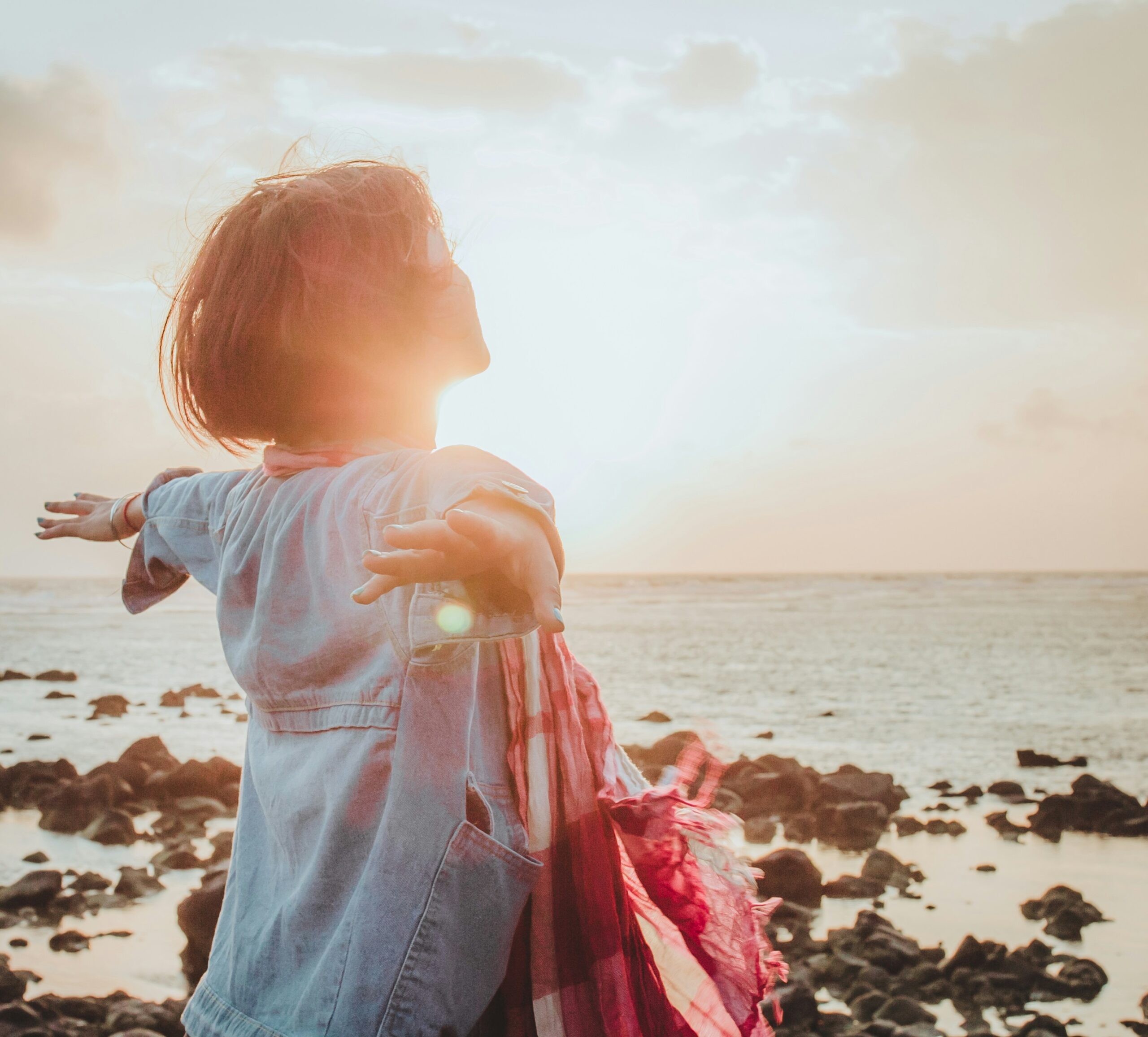 A child with open arms enjoying the seaside at sunset.